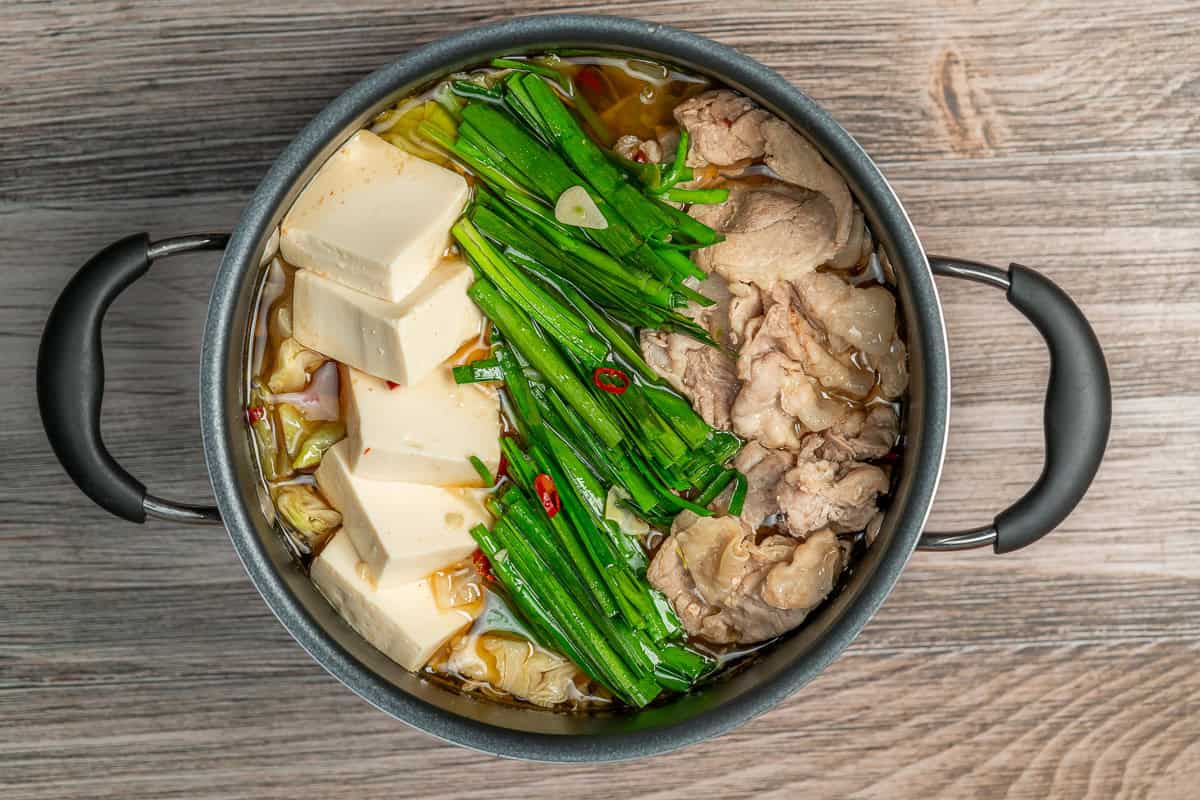 Pot of Pork Belly & Cabbage Nabe Hot Pot with tofu, nira and pork on a wood table