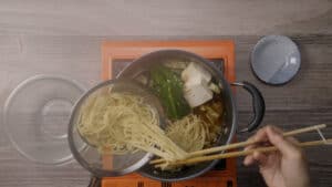 Adding ramen noodles to Pot with nira, tofu, cabbage, and tofu